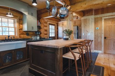 A wooden butcher block-topped island and metal hardware embolden the look of this Spokane log cabin.